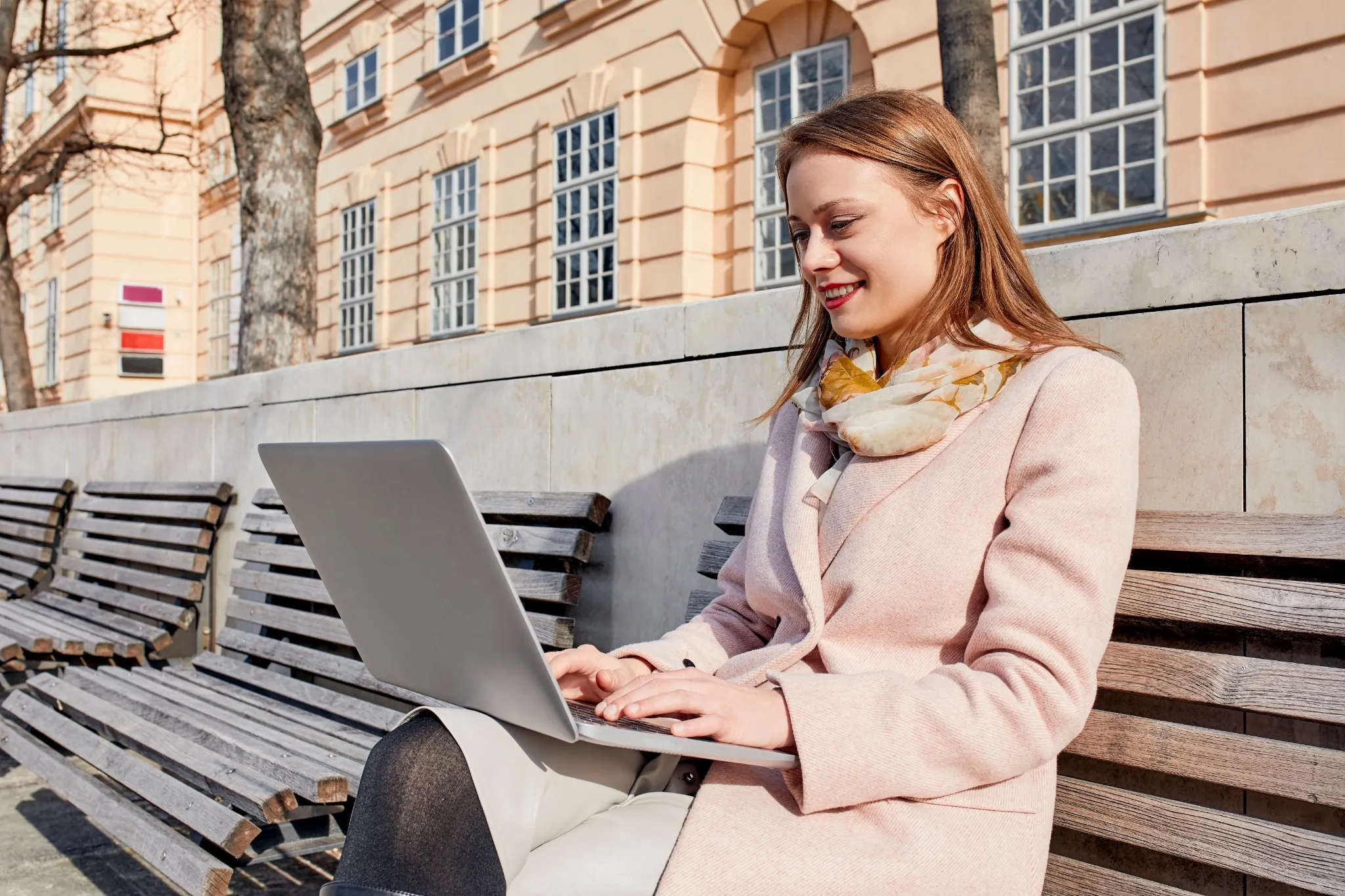 Austria, Vienna, smiling young woman sitting on bench at MuseumsQuartier using laptop
