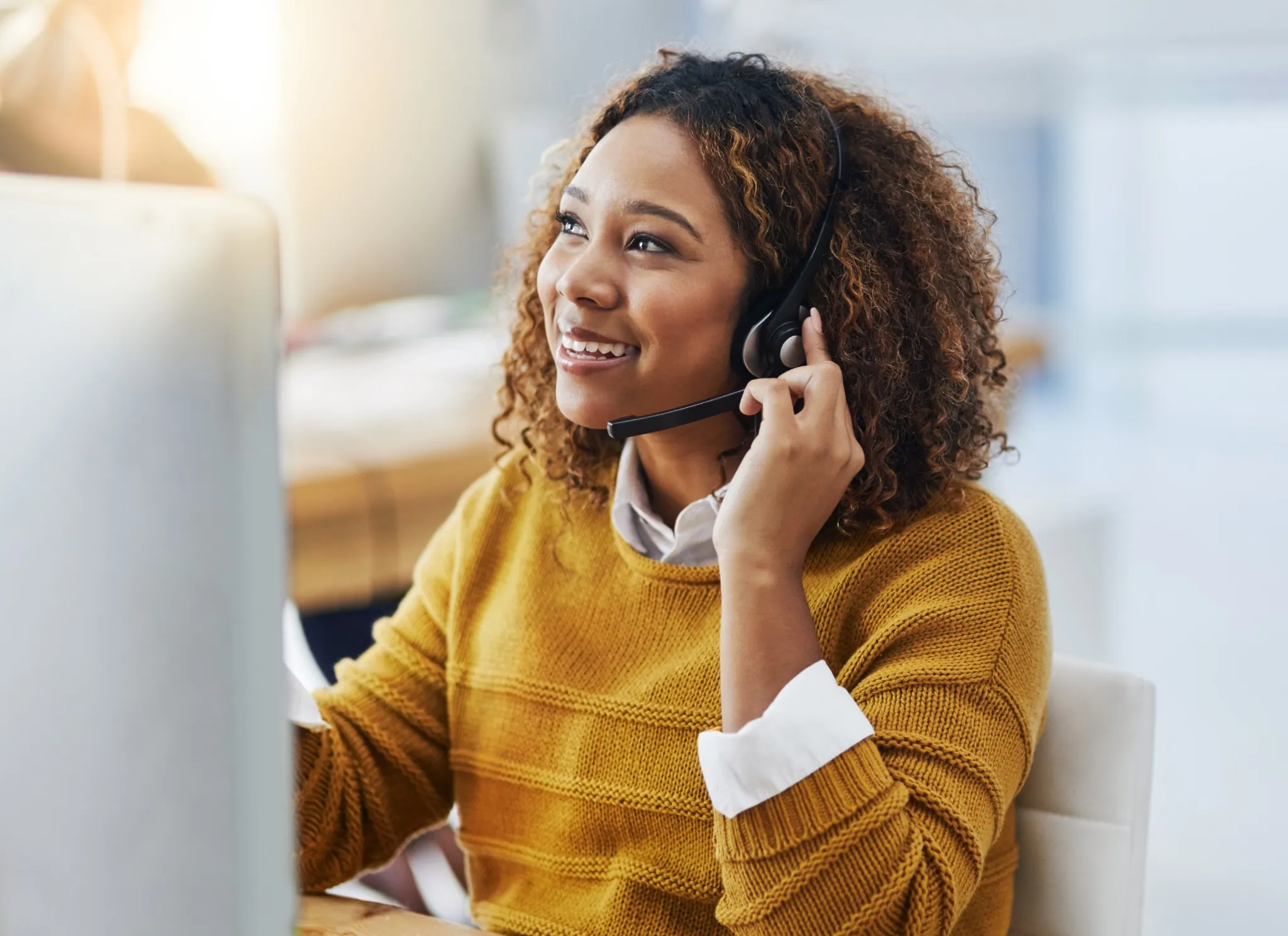 Friendly woman wearing headset talking with customer in front of computer screen