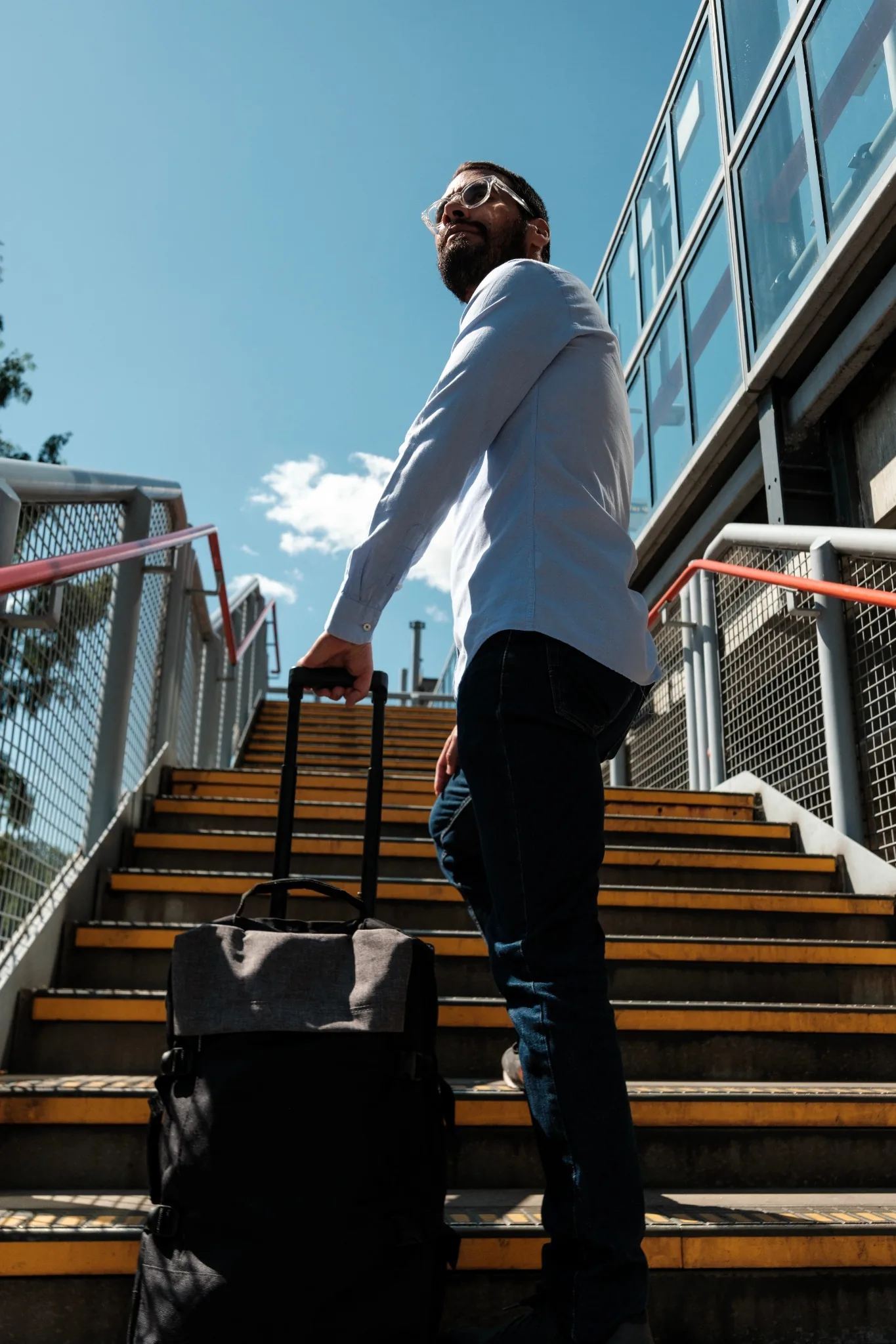 Business man standing on outdoor stairs with luggage in warm climate