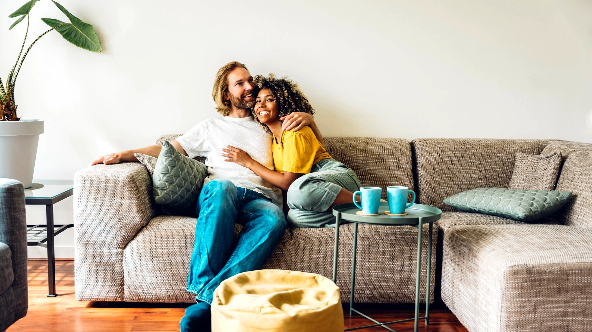 Happy mixed race couple cuddling on the couch with their coffee mugs