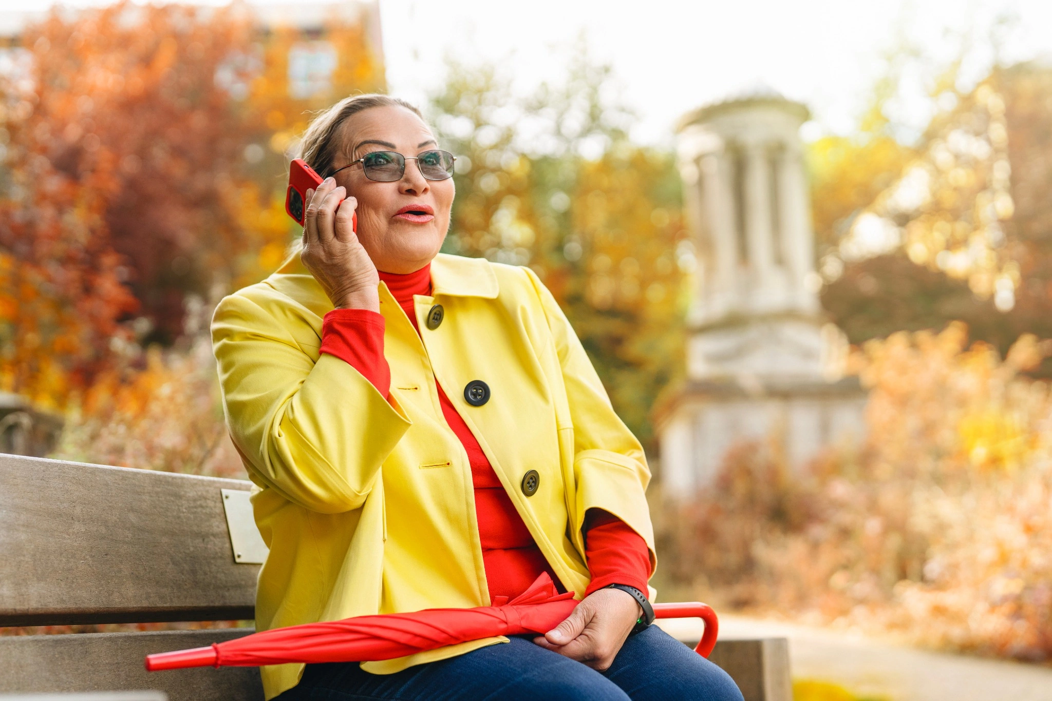 A woman wearing a bright-colored coat is talking on her phone while sitting on a park bench in Washington, D.