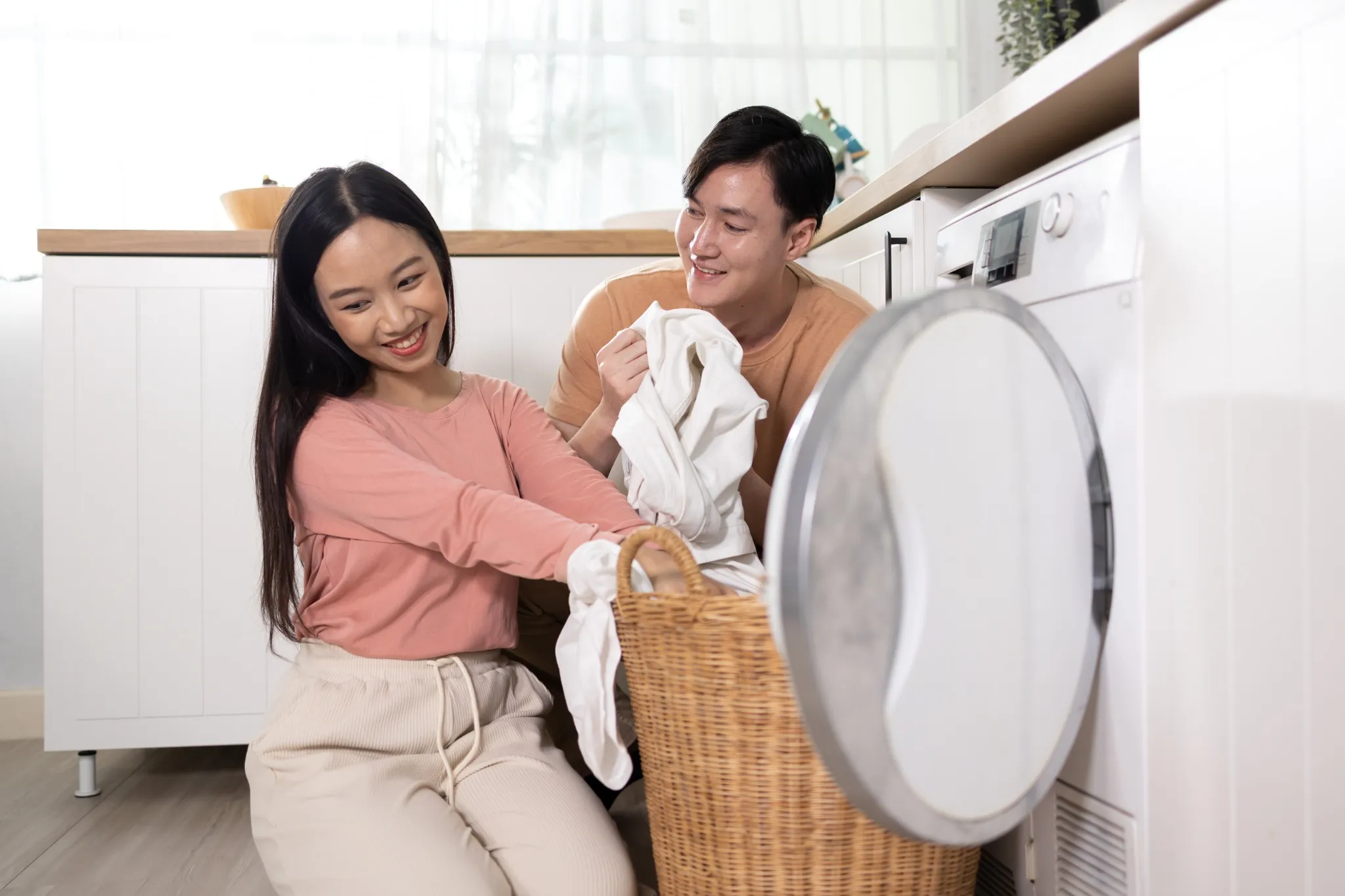 Young Asian married happy couple smiling and doing laundry at home.