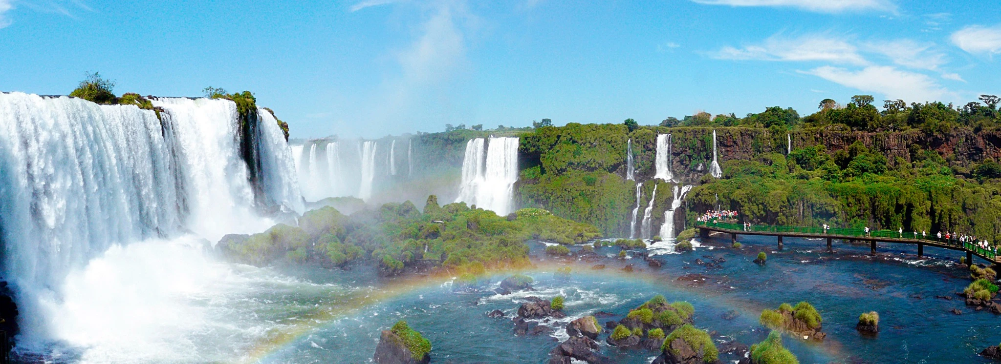 Iguacu falls in Argentina on a bright blue sky day with rainbow from mist