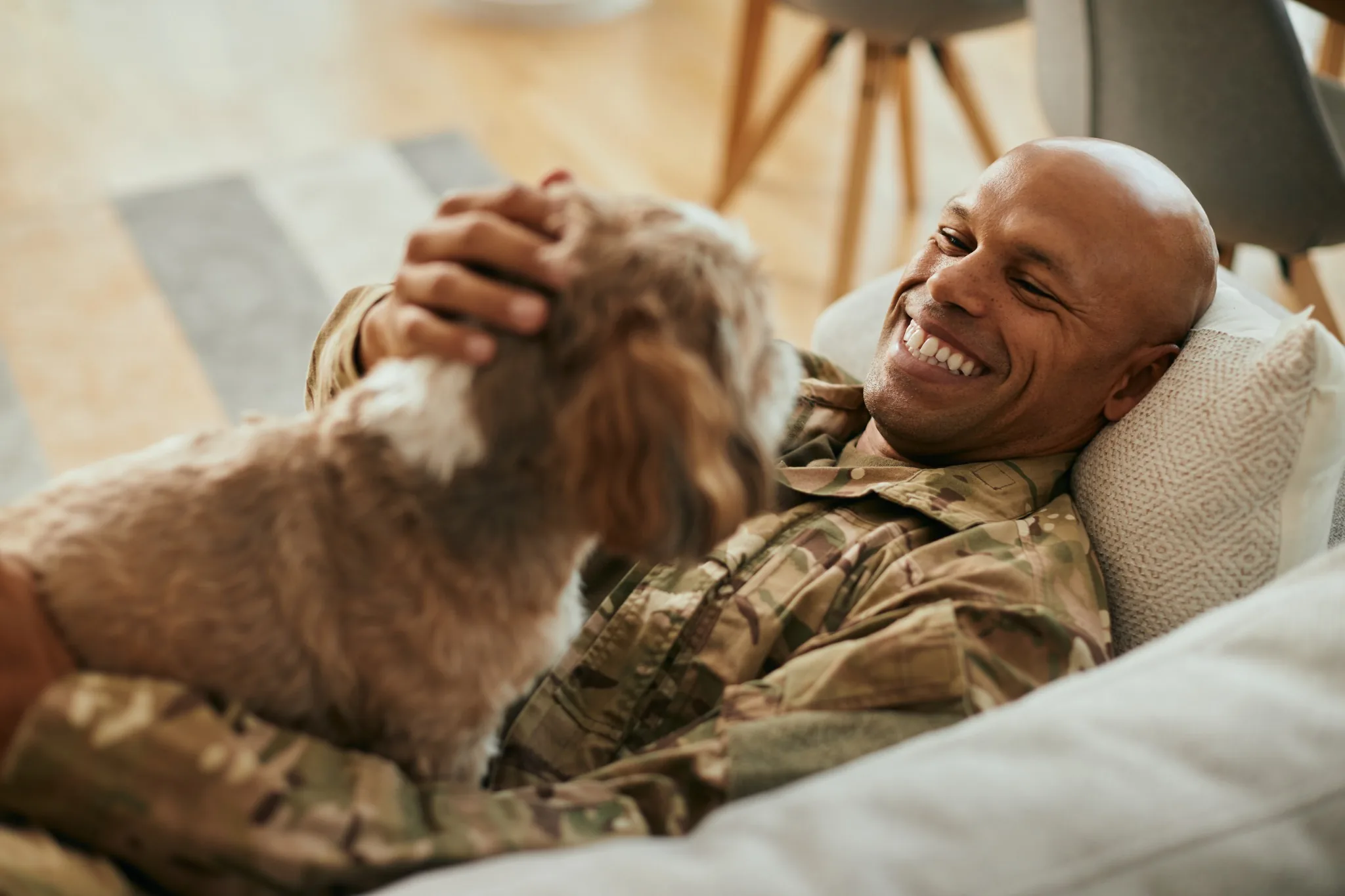 Military man laying on the couch smiling and petting small dog