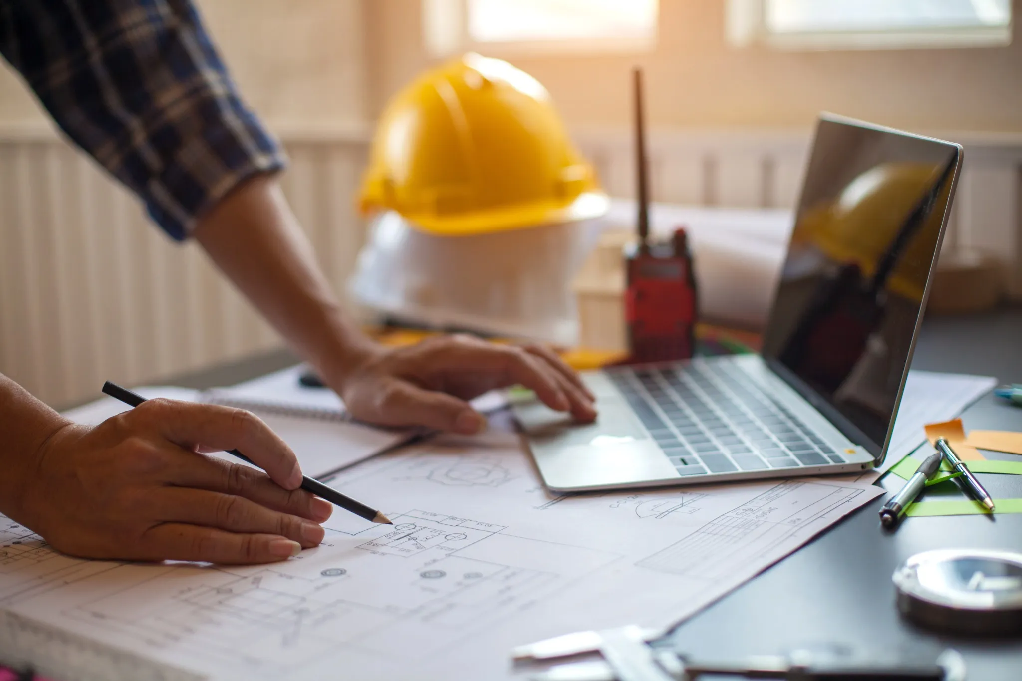 Construction engineer standing over desk with plans and laptop
