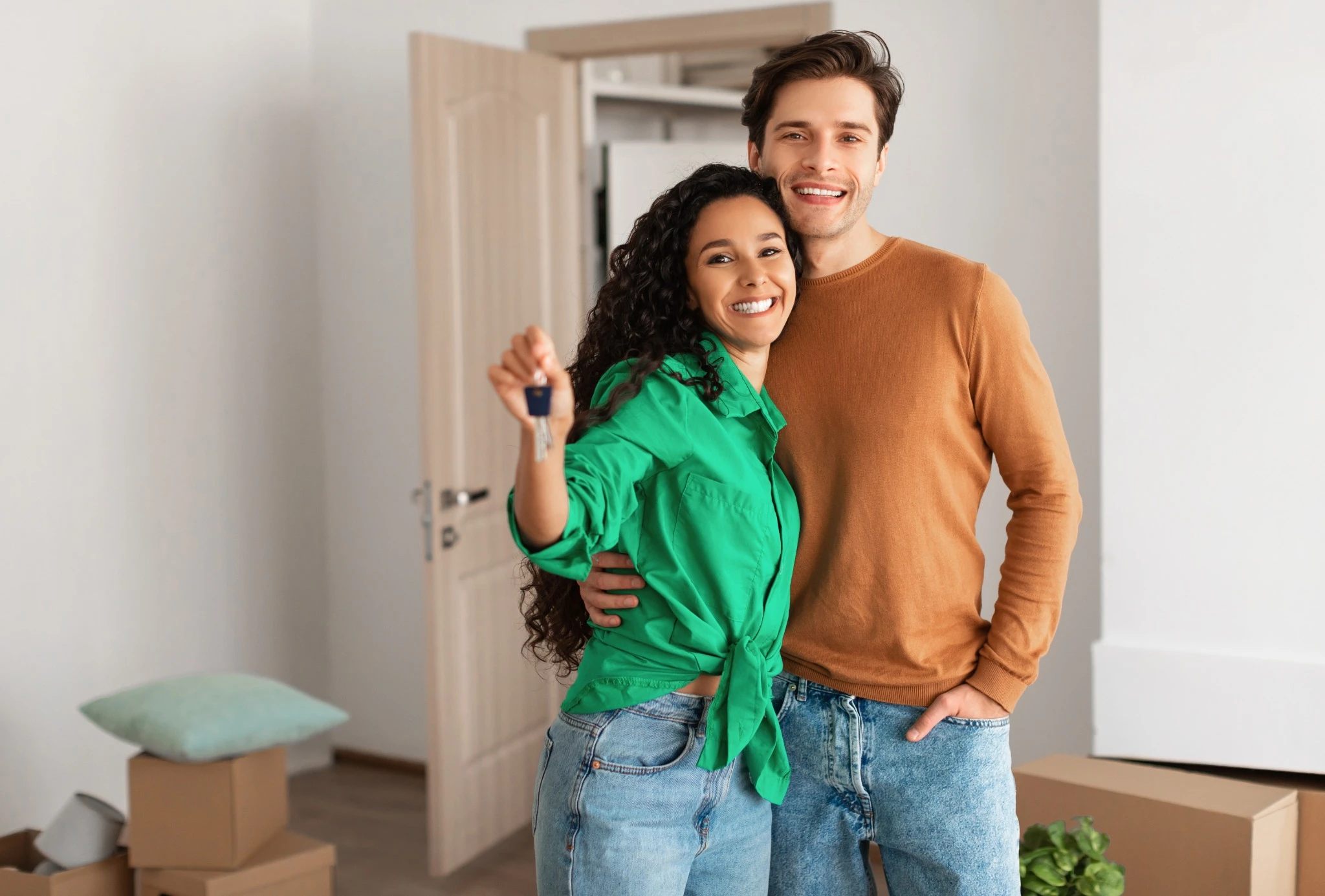 House Ownership. Portrait Of Happy Young Couple Holding Showing Key Standing In New Flat, Cheerful Guy Embracing Lady Posing After Moving In Own Apartment.