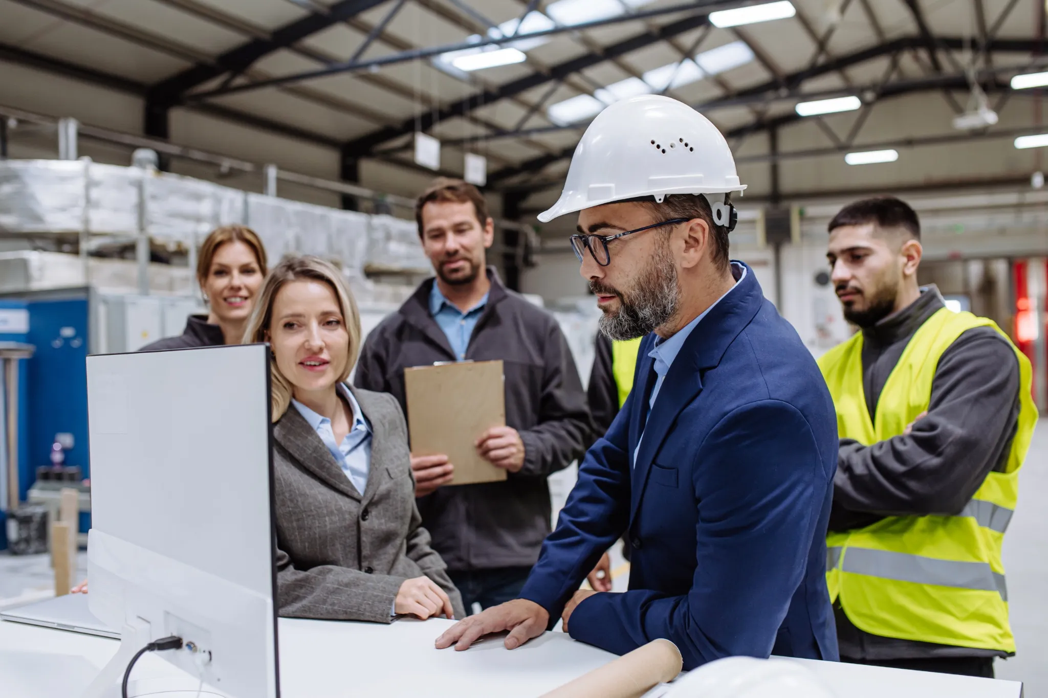 Manager presenting project to full team of warehouse employees on computer. Team of workers, managers, female director in modern industrial factory, heavy industry, manufactrury..