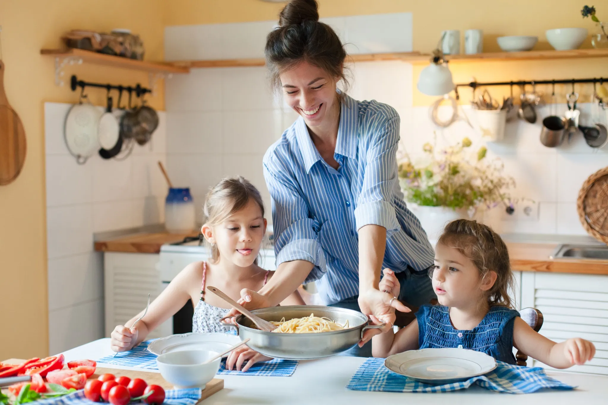 Happy mother serving pasta for daughters at home kitchen. Cozy family lunch, parenthood, comfort food, healthy eating for kids concept. Homemade Italian cuisine, mac and cheese.