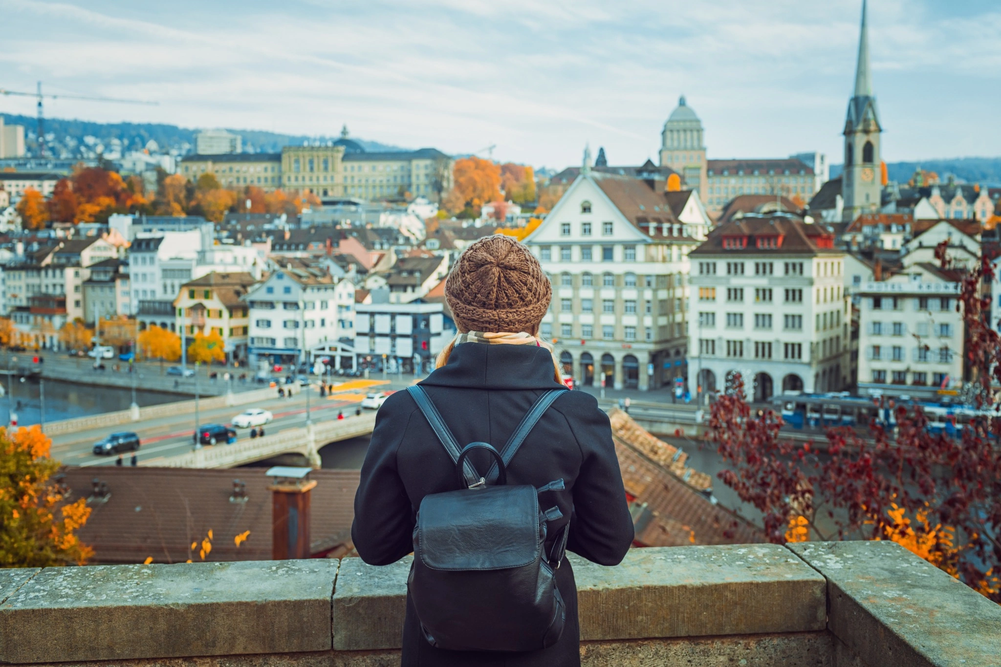 Young blonde tourist girl in warm hat and coat with backpack walking at cold autumn in Europe city enjoying her travel in Zurich Switzerland.