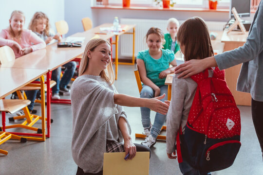 Little girl shaking hands with friendly teacher at new school