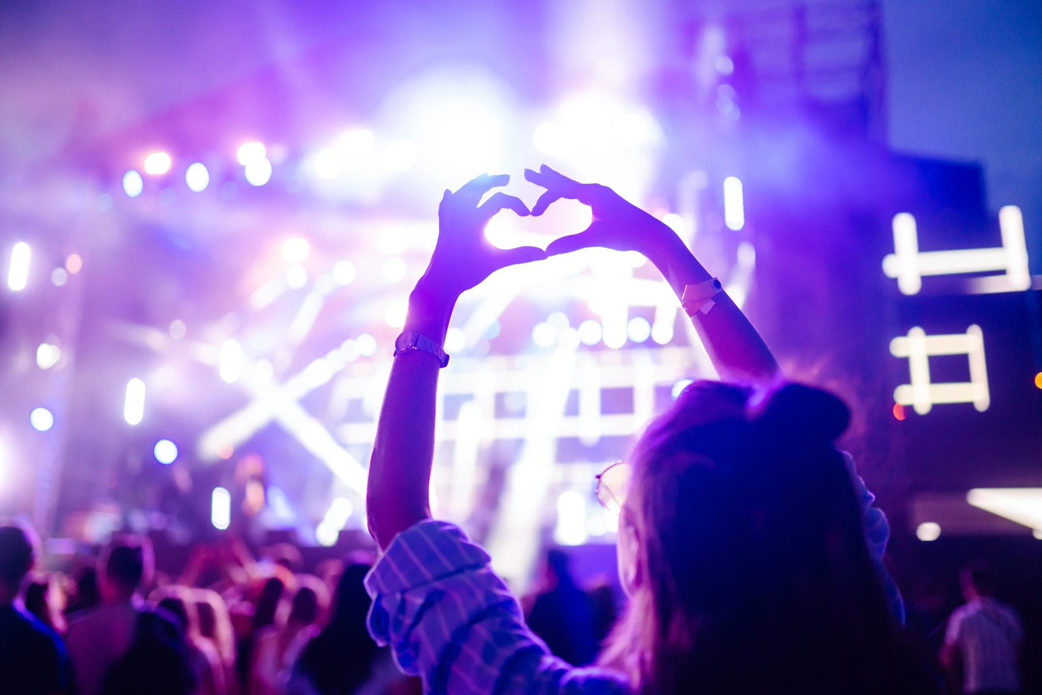Heart shaped hands at concert, loving the artist and the festival. Music concert with lights and silhouette of people enjoying the concert..jpg